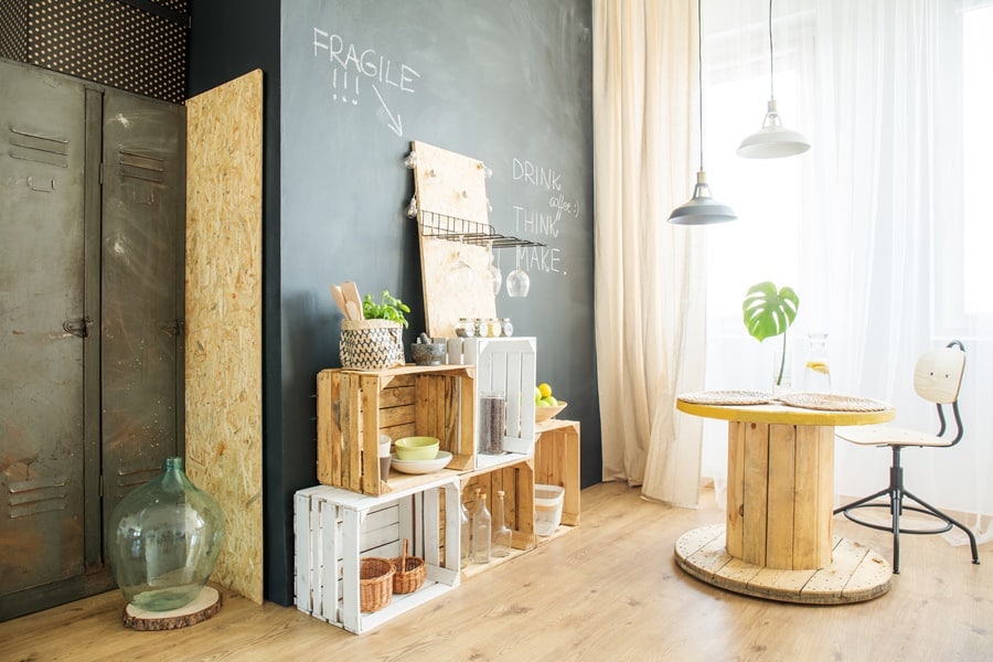 Rincón decorado con muebles reutilizados, cajas de fruta de madera y mesa hecha con bobina industrial, ejemplo de almacenamiento sostenible con conciencia ecológica.