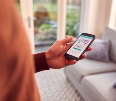 Uso de apps para el hogar en entorno moderno, con móvil en mano mostrando herramientas digitales para organizar tareas y espacios.