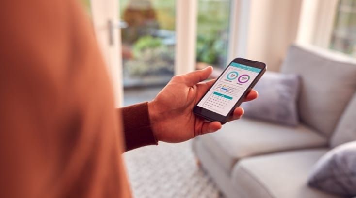 Uso de apps para el hogar en entorno moderno, con móvil en mano mostrando herramientas digitales para organizar tareas y espacios.