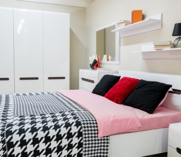 Dormitorio ordenado con cama de sábanas rosas, cojines oscuros y estanterías con libros, que transmite calma y muestra cómo el orden ayuda a reducir la ansiedad.