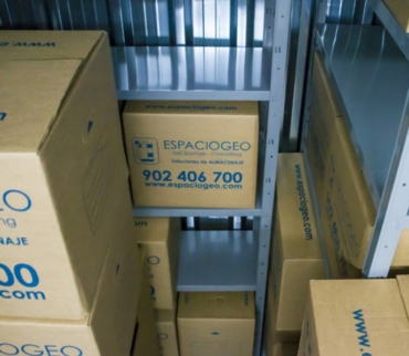 Cajas de cartón con el logo de ESPACIOGEO organizadas en estanterías metálicas dentro de un trastero. Ejemplo práctico de cómo organizar un trastero aprovechando cada rincón de forma eficiente.