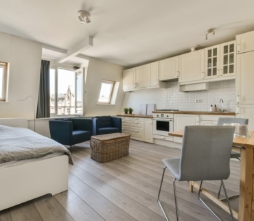 Espacio multifuncional en vivienda pequeña con cocina, zona de estar, cama y comedor integrados en un mismo ambiente luminoso.