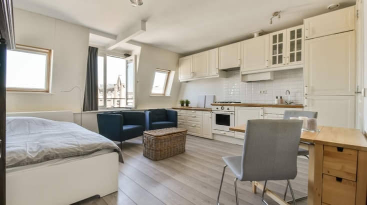 Espacio multifuncional en vivienda pequeña con cocina, zona de estar, cama y comedor integrados en un mismo ambiente luminoso.