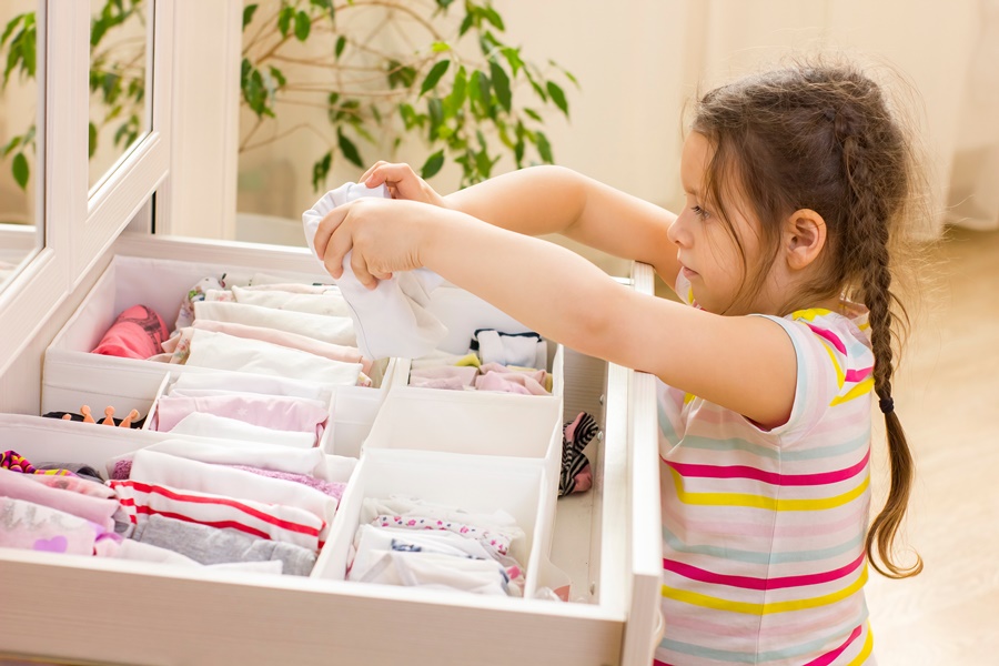 Niña doblando y organizando ropa interior en un cajón con divisores, representando buenos hábitos de orden para niños.