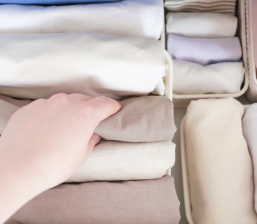 Mano seleccionando prendas dobladas verticalmente en un cajón, mostrando técnicas para doblar la ropa que optimizan el espacio y facilitan el orden diario.