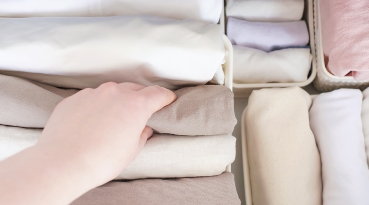 Mano seleccionando prendas dobladas verticalmente en un cajón, mostrando técnicas para doblar la ropa que optimizan el espacio y facilitan el orden diario.