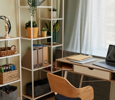 Zona luminosa de trabajo con estanterías, plantas y escritorio ordenado, ejemplo de organización del teletrabajo desde casa en espacios compartidos.