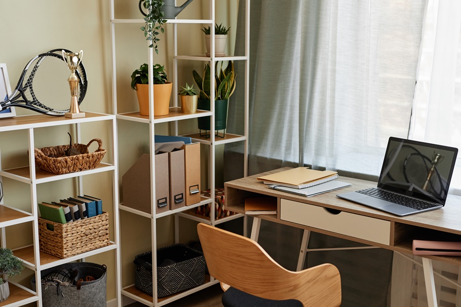 Zona luminosa de trabajo con estanterías, plantas y escritorio ordenado, ejemplo de organización del teletrabajo desde casa en espacios compartidos.
