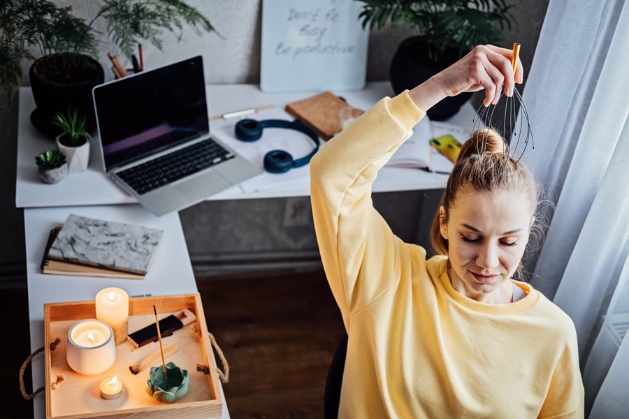 Mujer en pausa activa junto a escritorio con velas, portátil y objetos personales, representando equilibrio y bienestar en la organización del teletrabajo desde casa.