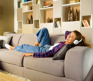 Mujer relajada escuchando música con auriculares mientras descansa sobre un sofá en un salón moderno y ordenado, transmitiendo bienestar asociado a la psicología del orden.