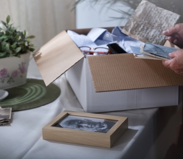 Persona mayor revisando cartas y fotografías antiguas junto a una caja abierta con objetos personales, en una escena íntima y ordenada, ejemplo de cómo conservar recuerdos sin saturar el hogar.