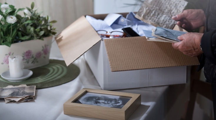 Persona mayor revisando cartas y fotografías antiguas junto a una caja abierta con objetos personales, en una escena íntima y ordenada, ejemplo de cómo conservar recuerdos sin saturar el hogar.