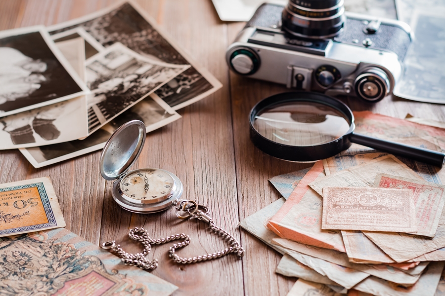 Mesa de madera con fotos antiguas, cámara retro, lupa y reloj de bolsillo, representando objetos sentimentales que muchas personas desean conservar como recuerdos valiosos.
