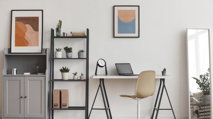 Zona de trabajo organizada con escritorio blanco, estantería vertical con plantas y cajas, y decoración sobria. Ejemplo visual de minimalismo práctico en espacios funcionales.
