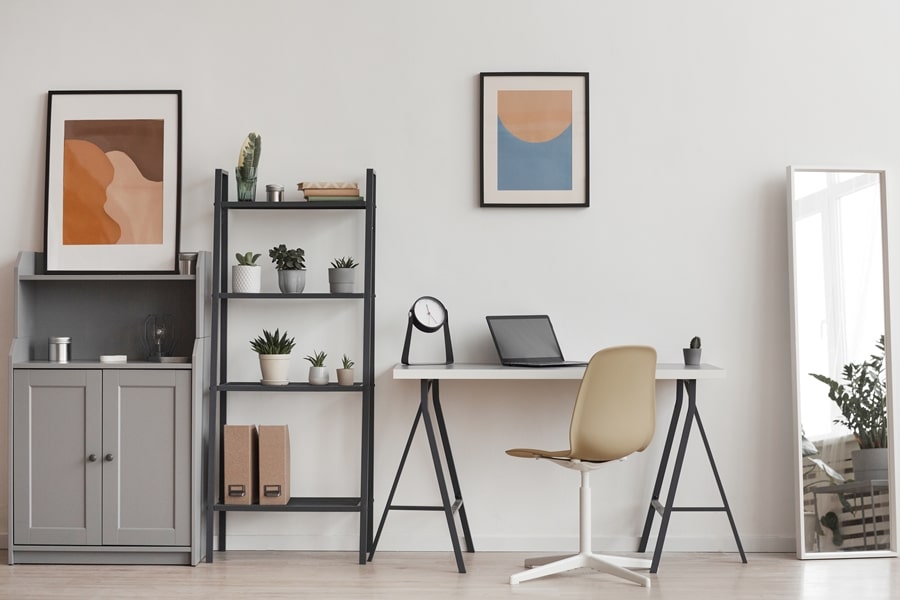 Zona de trabajo organizada con escritorio blanco, estantería vertical con plantas y cajas, y decoración sobria. Ejemplo visual de minimalismo práctico en espacios funcionales.