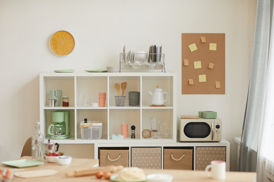 Cocina compartida organizada con estanterías blancas, vajilla, microondas y cafetera, perfecta para aplicar reglas de orden en piso compartido.
